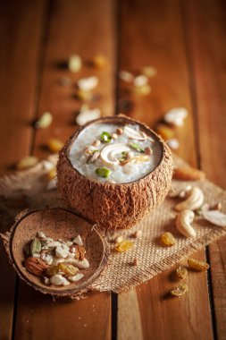 Kuru meyvelerle süslenmiş kremalı Sabudana Kheer 'in yakın çekimi. Hint usulü lezzetli tatlı. Hindistan cevizi kabuğunda servis edilmiş. Ahşap arkaplanda ön görünüm.