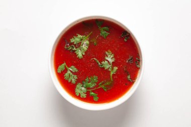 Hindistan ev yapımı taze domates çorbası taze kişniş yaprakları ve kuru nane veya fesleğen yapraklarıyla süslenmiş, seramik beyaz bir kasede servis edilir.