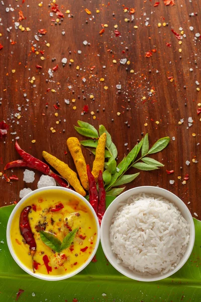 Close-up of Indian cooked rice with kadi or kadhi over the banana fresh green leaf. Garnished with curry-patta leaves and red chilli paper and salt.