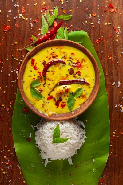 Close-up of Indian cooked rice with kadi or kadhi over the banana fresh green leaf. Garnished with curry-patta leaves and red chilli paper and salt.