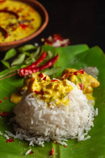 Close-up of Indian cooked rice with kadi or kadhi over the banana fresh green leaf. Garnished with curry-patta leaves and red chilli paper and salt.