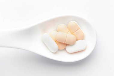 Macro, beyaz seramik kaşıkla tıbbi ya da bitkisel hafif sarı tableti kapat. Üst görünüm, beyaz arkaplan.