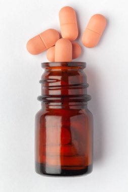 Macro. İlaç ya da bitkisel hafif pembe hapları hapın içine dök ve kehribar cam bir şişeye koy. Üst görünüm, beyaz arkaplan.