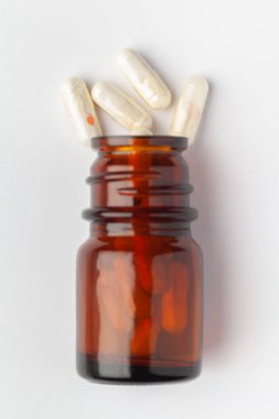 Macro. İlaç ya da bitkisel beyaz kapsülün içine dökülen hapları ve kehribar cam bir şişeyi kapat. Üst görünüm, beyaz arkaplan.