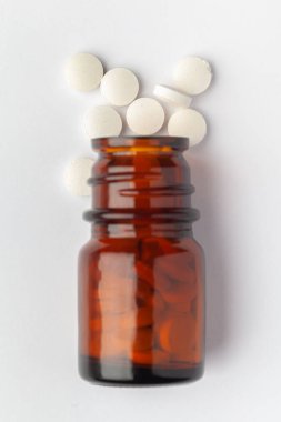 Makro... Tıbbi ya da bitkisel beyaz hap dökülmüş ve kehribar cam bir şişeye dökülmüş. Üst görünüm, beyaz arkaplan.