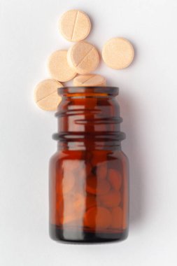 Macro. İlaç ya da bitkisel hafif sarı tableti hapın içine dök ve kehribar cam bir şişeye koy. Üst görünüm, beyaz arkaplan.