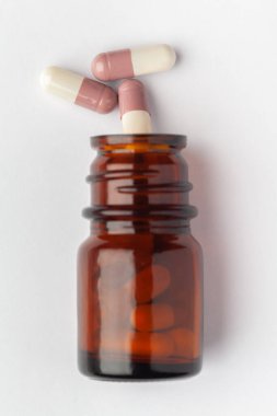 Macro... Tıbbi ya da bitkisel beyaz kahverengi kapsülün kapsülleri kehribar cam bir şişeye dökülmüş. Üst görünüm, beyaz arkaplan.