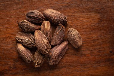 Ahşap arka planda organik siyah kakule (Amomum subulatum) yakın çekim. Hint Aromatik Baharatı Yığını. Üst görünüm