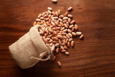 Organik Lobiye yakın plan, ya da tahtadan kahverengi arka plan üzerine döşeme jüt çantasından dökülen fasulye dalıyla..