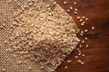 Organik Beyaz Susam Tohumlarının Makro Yakın Çekimi (Sesamum indicum) veya Jute minderi ve ahşap kaplama kabuklu beyaz Til.