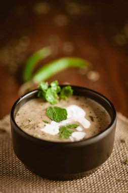 Methi-Matar-Malai 'nin taze yeşil biber, nane yaprağı ve soğanlı beyaz körili yakın çekimi. Popüler, lezzetli bir Hint tarifi, siyah bir kasede, ahşap arka planda..