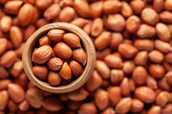 Macro Close-up of organic red-brown peanuts (Arachis hypogaea)  in an earthen clay pot (kulhar) on the self background. Top view