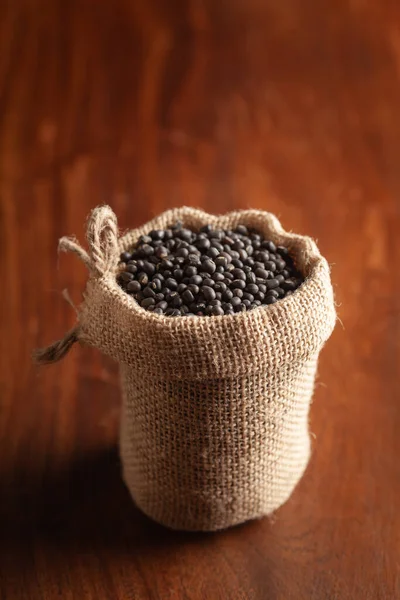 有機黒グラム Vigna Mungo または木製の茶色の背景の上に立った正しい袋の中の全体の黒ウラドのクローズアップ — ストック写真