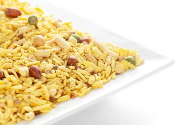 Fıstık, şeker, kuru üzüm ve besan sev ile yapılmış beyaz seramik kare tabakta lezzetli Khatta Meetha. Hindistan baharatlı çerez yığını (Namkeen), arka plan ışığı altında, yan görüş