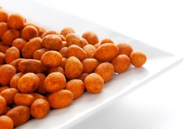 Beyaz seramik kare tabakta Çıtır Fıstık, besan kaplı fıstıkla yapılmış. Hindistan baharatlı çerez yığını (Namkeen), arka plan ışığı altında, yan görünüm, beyaz arka plan karşı.