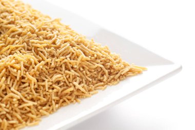 Beyaz seramik kare tabakta tuzlu düzlem Bhujia, nohut veya gram undan (Besan) yapılır. Hindistan tuzlu çerez yığını (Namkeen), arka plan ışığı altında, yan görünüm