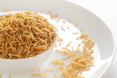 Hint baharatlı atıştırmalıkları (Namkeen) - Bikaneri Besan Bhujia beyaz bir kase içinde, nohut unundan (Besan) yapılmış, kenar manzaralı, beyaz arka planda.