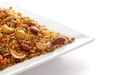 Fıstık, kaju, mısır gevreği, badem vs. ile yapılmış beyaz seramik bir tabakta 'Shahi Mixture'. Hint baharatlı atıştırmalıkları (Namkeen). Beyaz arkaplana karşı yan görünüm