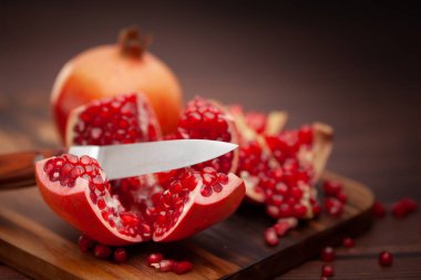 Tahta tahtada, ahşap zemin üzerinde bıçakla organik kırmızı nar tohumu (Punica granatum) yakın plan..