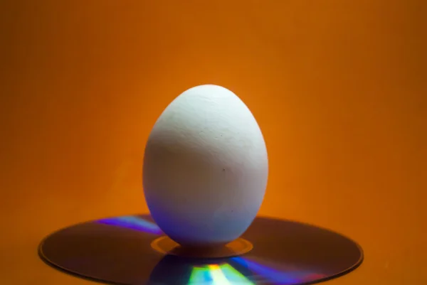 Huevo blanco en un CD con fondo naranja — Foto de Stock