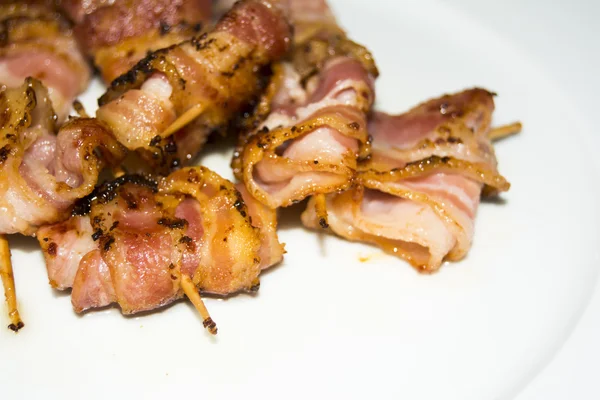 Rolls of slices of cooked bacon subject with a toothpick — Stock Photo, Image