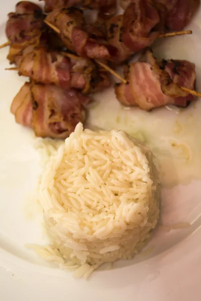 Rice with Rolls of slices of cooked bacon subject with a toothpi — Stock Photo, Image