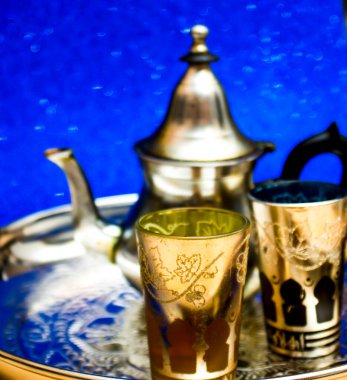 Bir grup çaydanlık ve bir bardak oryantal çay mavi arka plandaki bir tepside parlıyor.