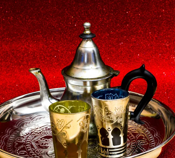 Group of teapot and glasses of oriental tea on a tray on red background with glitter