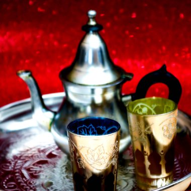 Bir grup çaydanlık ve bir bardak oryantal çay kırmızı arka planda parlayan bir tepside.