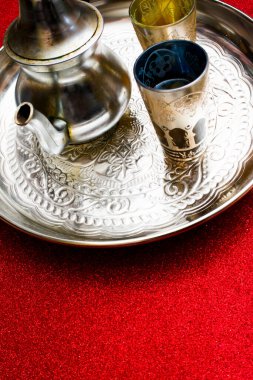 Bir grup çaydanlık ve bir bardak oryantal çay kırmızı arka planda parlayan bir tepside.