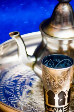 Bir grup çaydanlık ve bir bardak oryantal çay mavi arka plandaki bir tepside parlıyor.