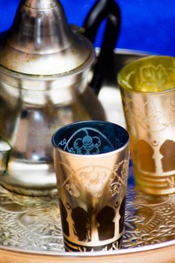 Bir grup çaydanlık ve bir bardak oryantal çay mavi arka plandaki bir tepside parlıyor.