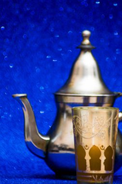 Bir grup çaydanlık ve bir bardak oryantal çay mavi arka plandaki bir tepside parlıyor.