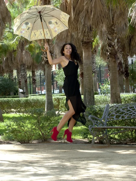 Mooie vrouw springen in een park met paraplu — Stockfoto
