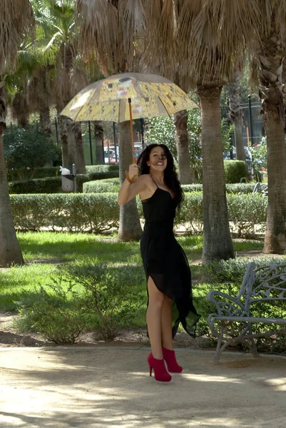 Mooie vrouw springen in een park met paraplu — Stockfoto