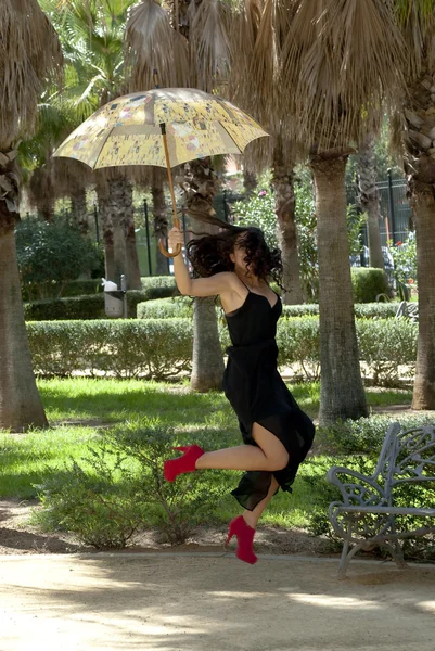 Mooie vrouw springen in een park met paraplu — Stockfoto