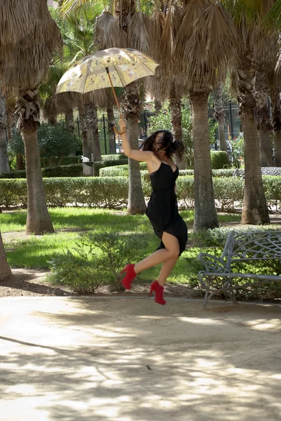 Mooie vrouw springen in een park met paraplu — Stockfoto