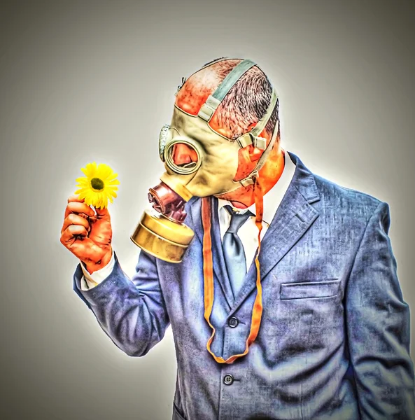 Businessman with gas mask looking at an flower in his hand retou — Stock Photo, Image