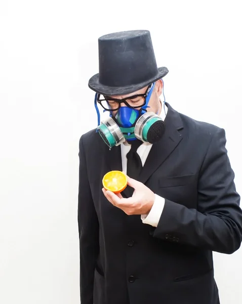 Empresario con máscara de gas y sombrero mirando una naranja — Foto de Stock