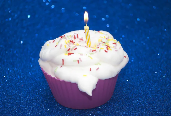 Cupcake com uma vela acesa sobre fundo azul brilhante — Fotografia de Stock