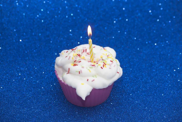 Cupcake con una vela encendida sobre fondo azul brillante — Foto de Stock