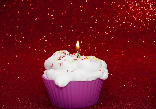 Cupcake con una vela encendida sobre fondo rojo brillante — Foto de Stock