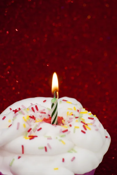 Cupcake com uma vela acesa sobre fundo vermelho brilhante — Fotografia de Stock