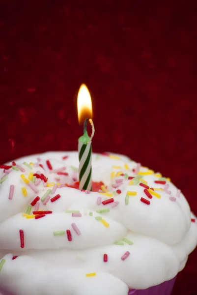 Cupcake con una vela encendida sobre fondo rojo brillante — Foto de Stock