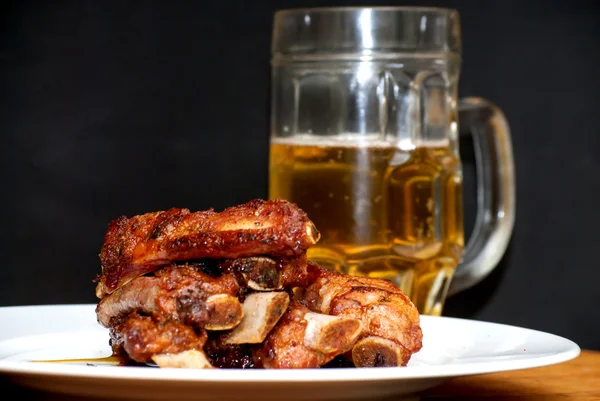 Costeletas de porco assadas em um prato branco com um jarro de cerveja ao lado — Fotografia de Stock