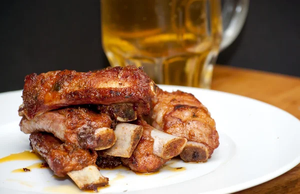 Costillas de cerdo asadas en un plato blanco con una jarra de cerveza al lado — Foto de Stock