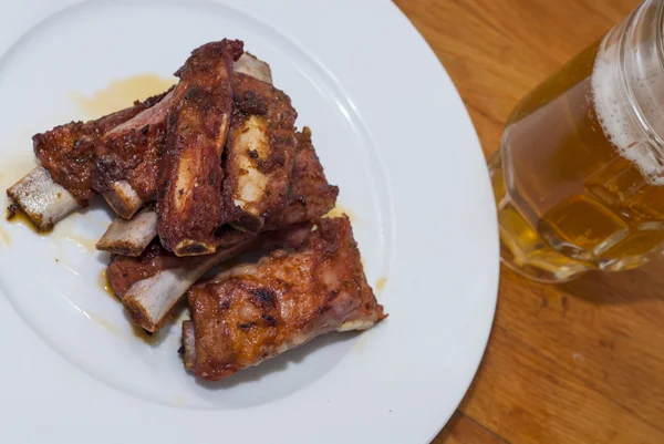 Costolette di maiale arrosto su un piatto bianco con una brocca di birra accanto — Foto Stock