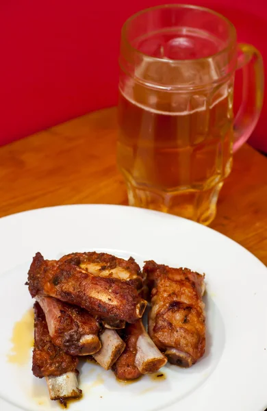 Costeletas de porco assadas em um prato branco com um jarro de cerveja ao lado — Fotografia de Stock