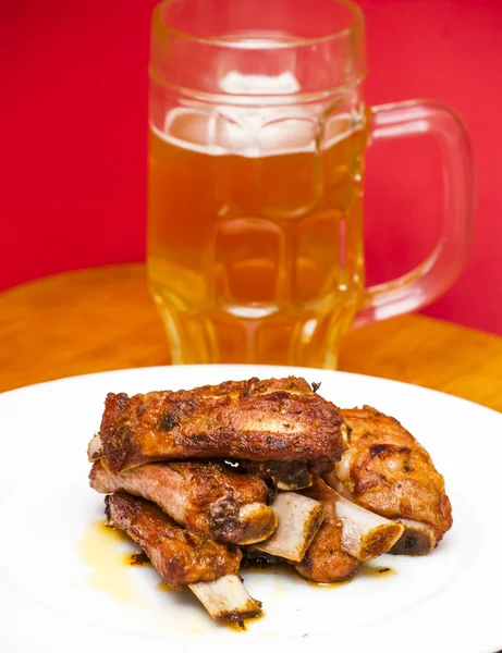 Costeletas de porco assadas em um prato branco com um jarro de cerveja ao lado — Fotografia de Stock