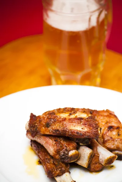 Roasted pork ribs on a white plate with a pitcher of beer next — Stock Photo, Image